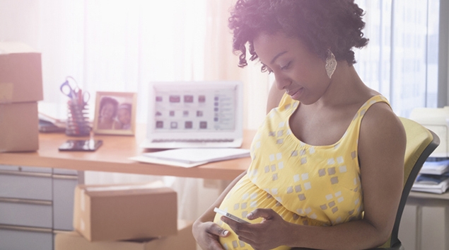 A pregnant Black woman looks at a phone screen