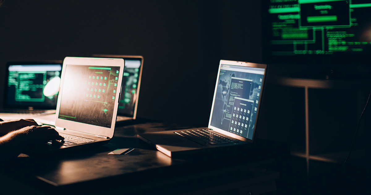 Person working on a laptop with multiple laptops and wall monitor