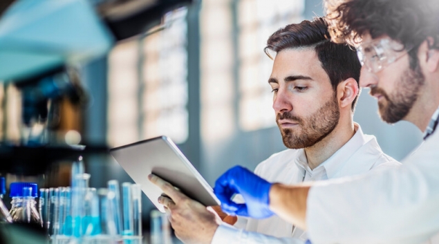 Lab worker pointing to table screen held by other worker