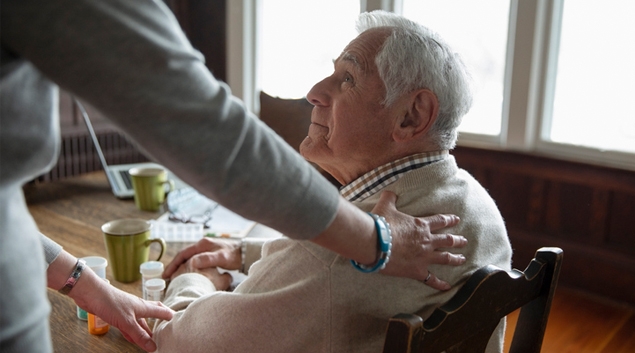 Senior man sitting at a table with woman's hand on his shoulder