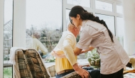 A nurse helps a resident into a chair.