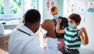 Child raises arms as he's seen by a doctor.