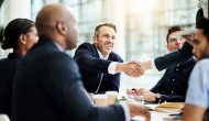 A handshake at a conference table with people in professional garb